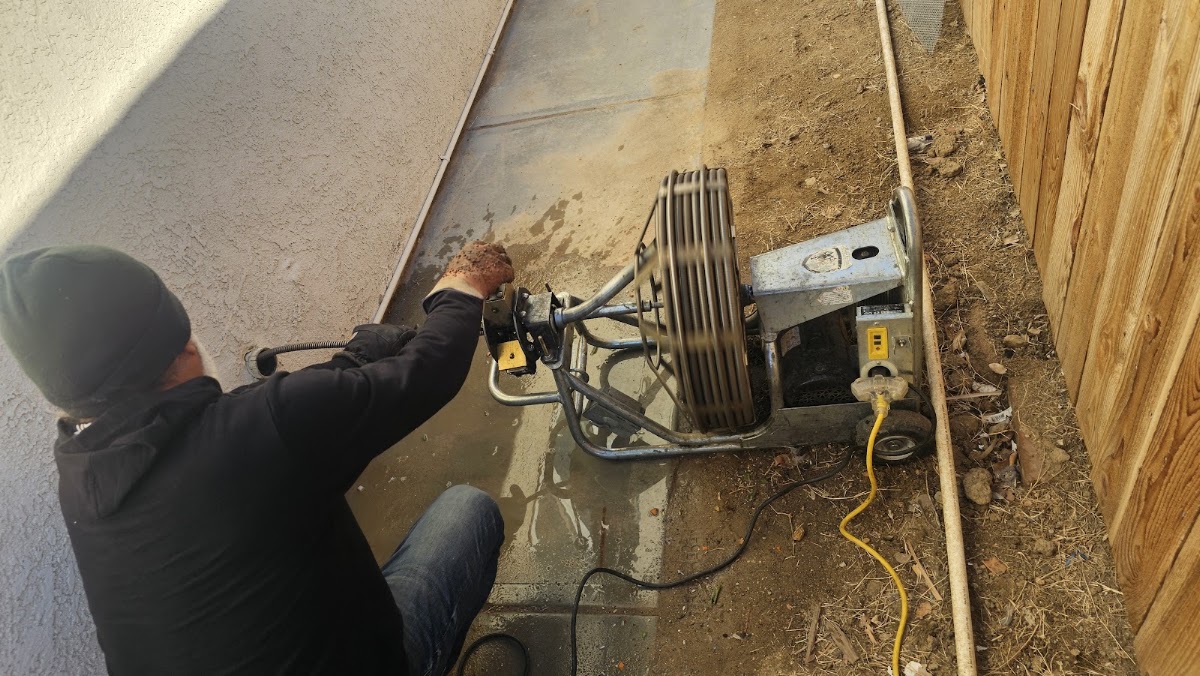 Gilbert running a sectional drain machine on a sewer line beside a house in Rosamond